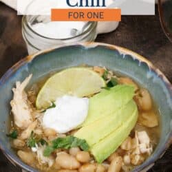 a bowl of white chicken chili topped with slices of avocado and sour cream.