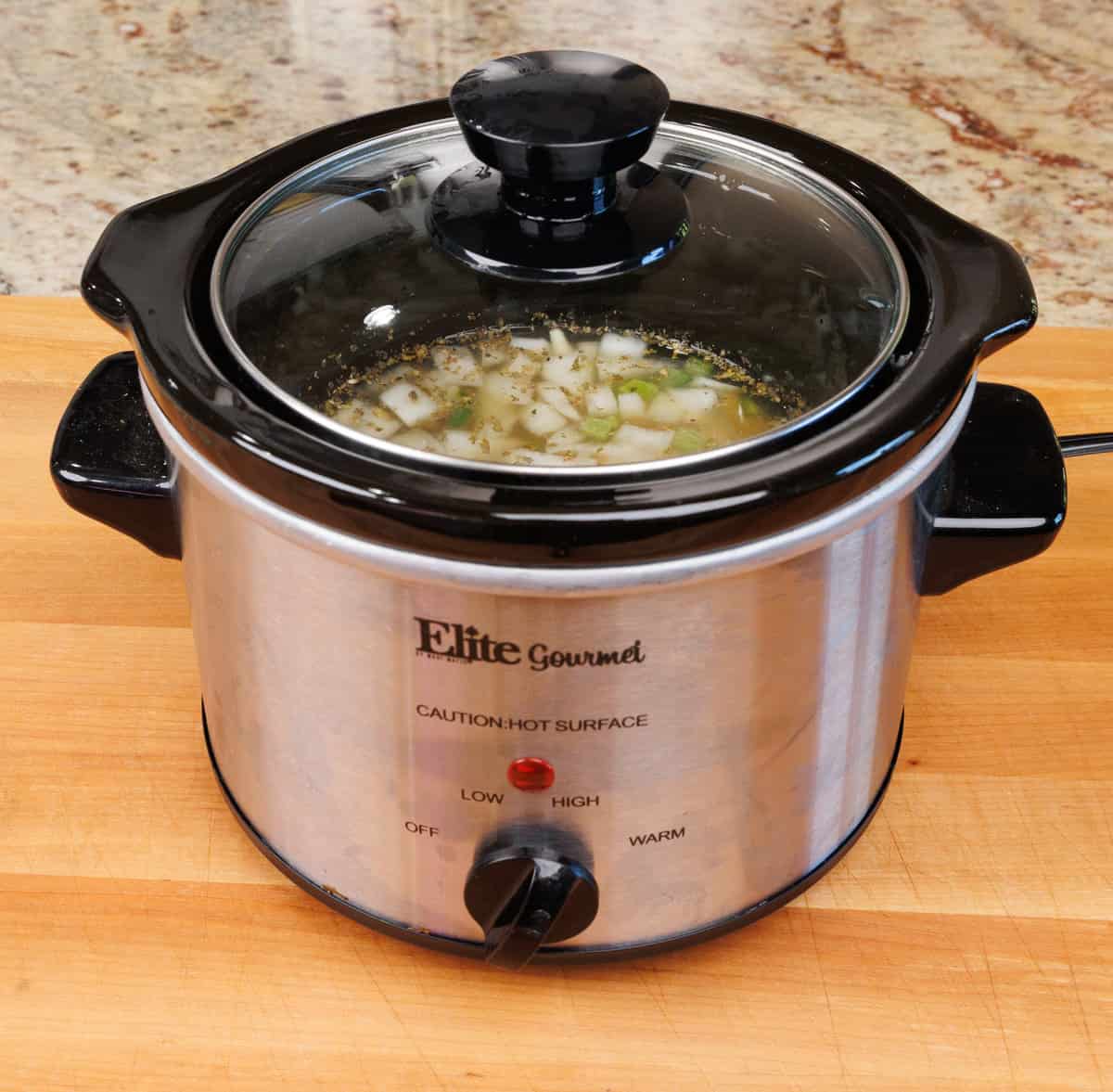 a small crockpot filled with chicken, onions, broth, and beans.