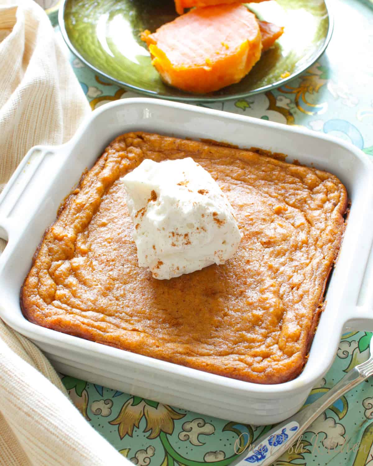a small sweet potato pie in a square baking dish next to a plate of sliced sweet potatoes.