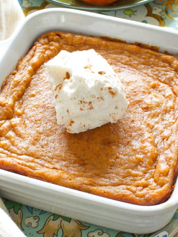 a small sweet potato pie in a square baking dish next to a plate of sliced sweet potatoes.