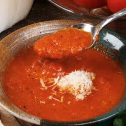 a spoonful of tomato soup over the bowl next to a brown napkin