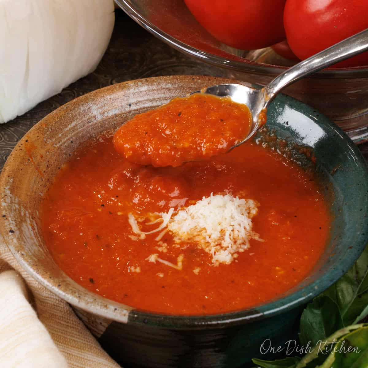 a bowl of homemade tomato basil soup topped with parmesan cheese on a silver tray.