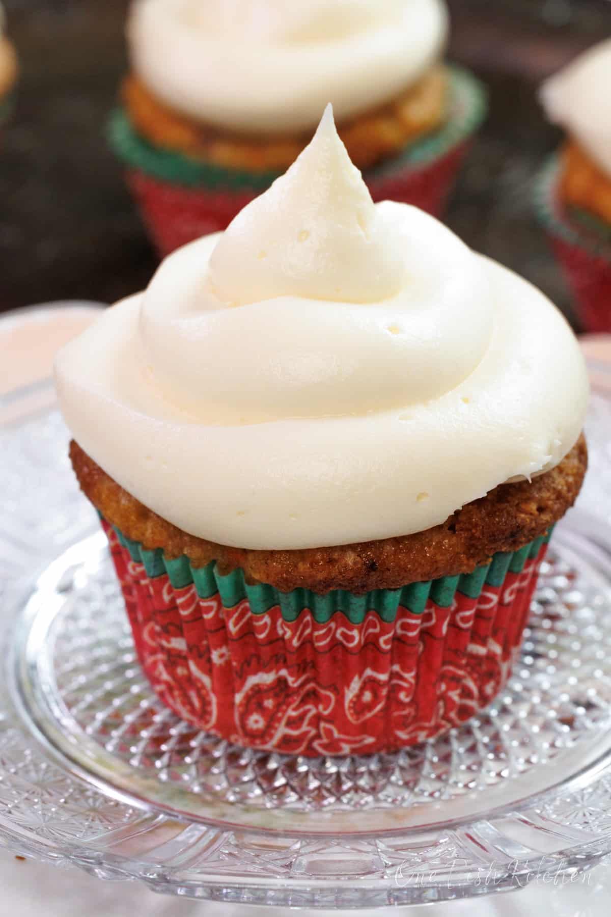 a carrot cake cupcake topped with cream cheese frosting on a white plate.