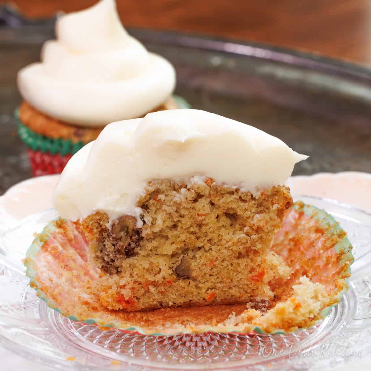 a single carrot cake cupcake topped with cream cheese frosting sliced in half on a plate.