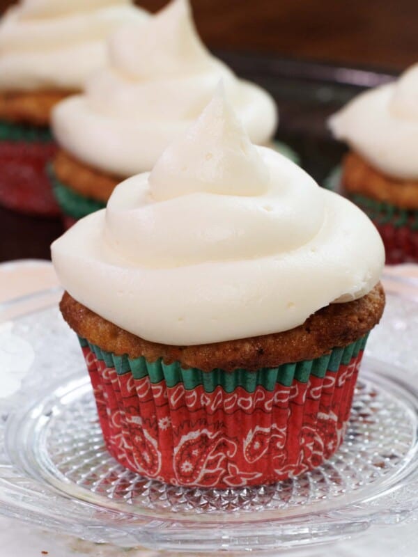one frosted carrot cake cupcake on a white plate next to three cupcakes