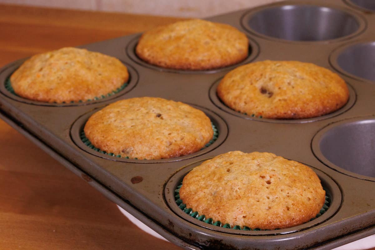 carrot cake cupcakes in muffin tins cooling on a kitchen counter