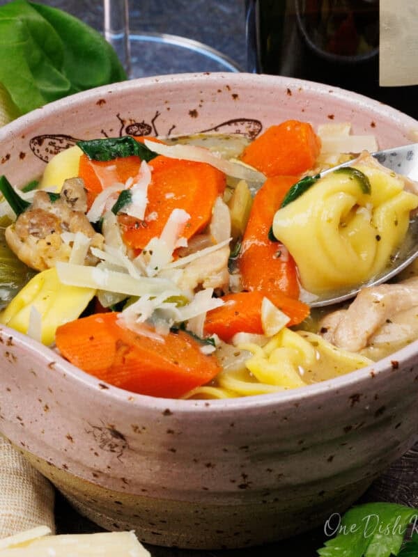 chicken tortellini soup in a bowl with a spoon on the side.