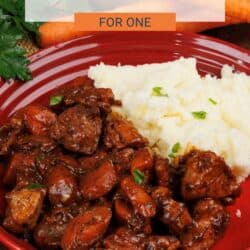 coq au vin in a red bowl next to a serving of mashed potatoes.