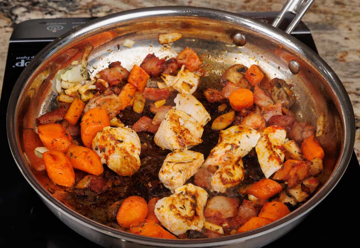 chicken pieces and vegetables cooking in a skillet