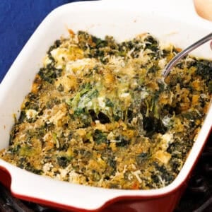 A small creamed spinach casserole in a red baking dish next to a blue napkin.