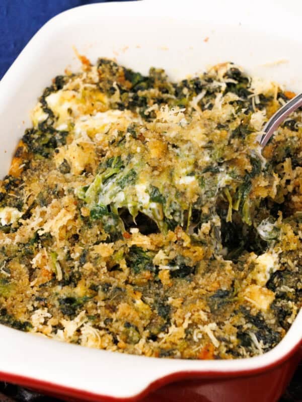 A small creamed spinach casserole in a red baking dish next to a blue napkin.