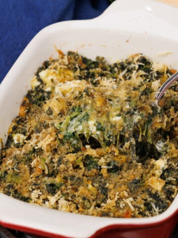 a small red baking dish filled with creamed spinach with a spoon on the side