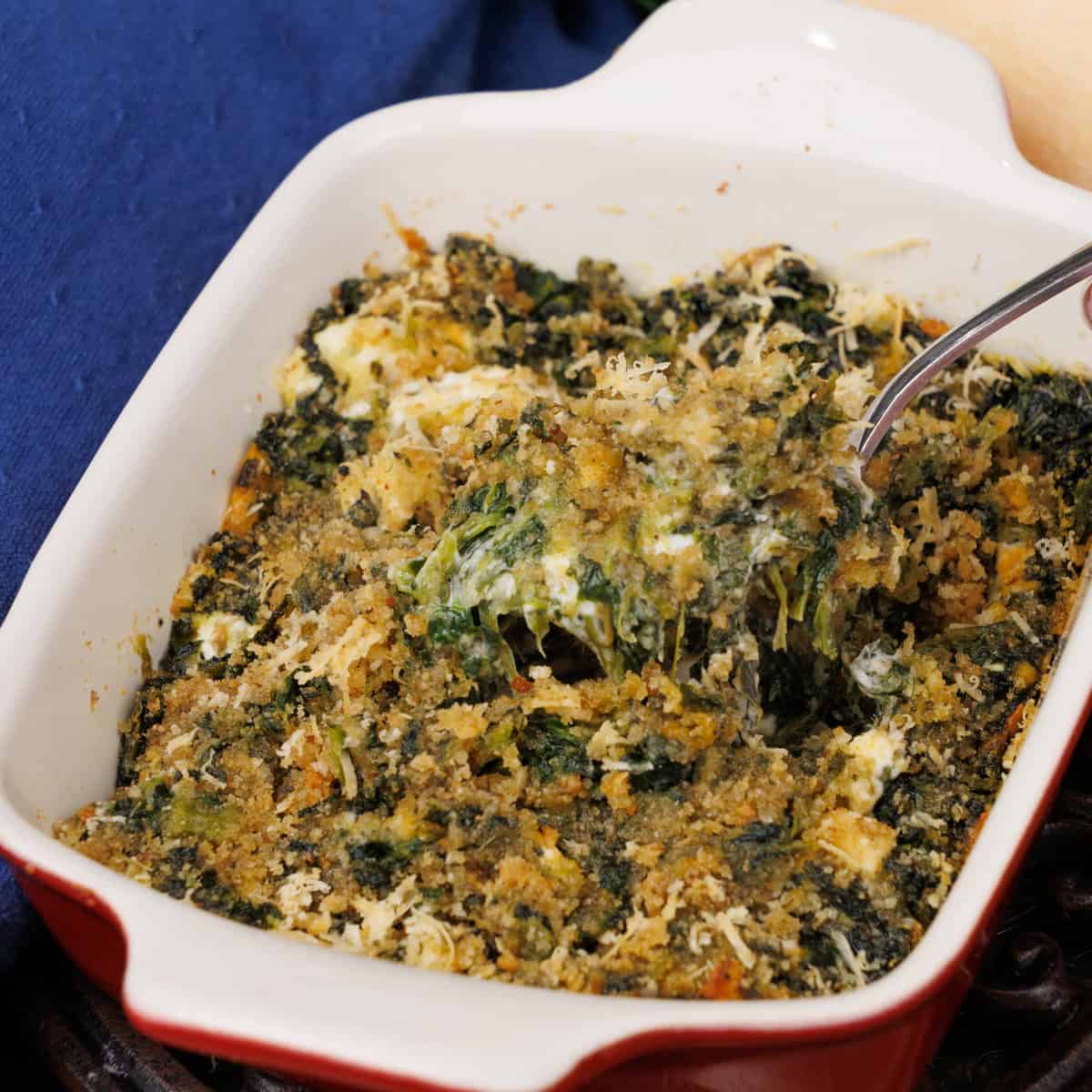 a small red baking dish filled with creamed spinach with a spoon on the side