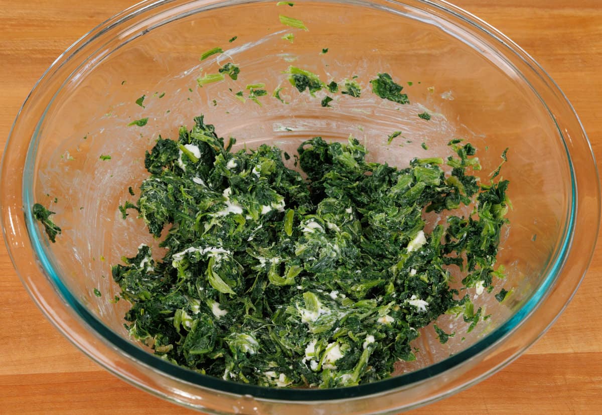 frozen and thawed spinach with cream cheese in a mixing bowl.