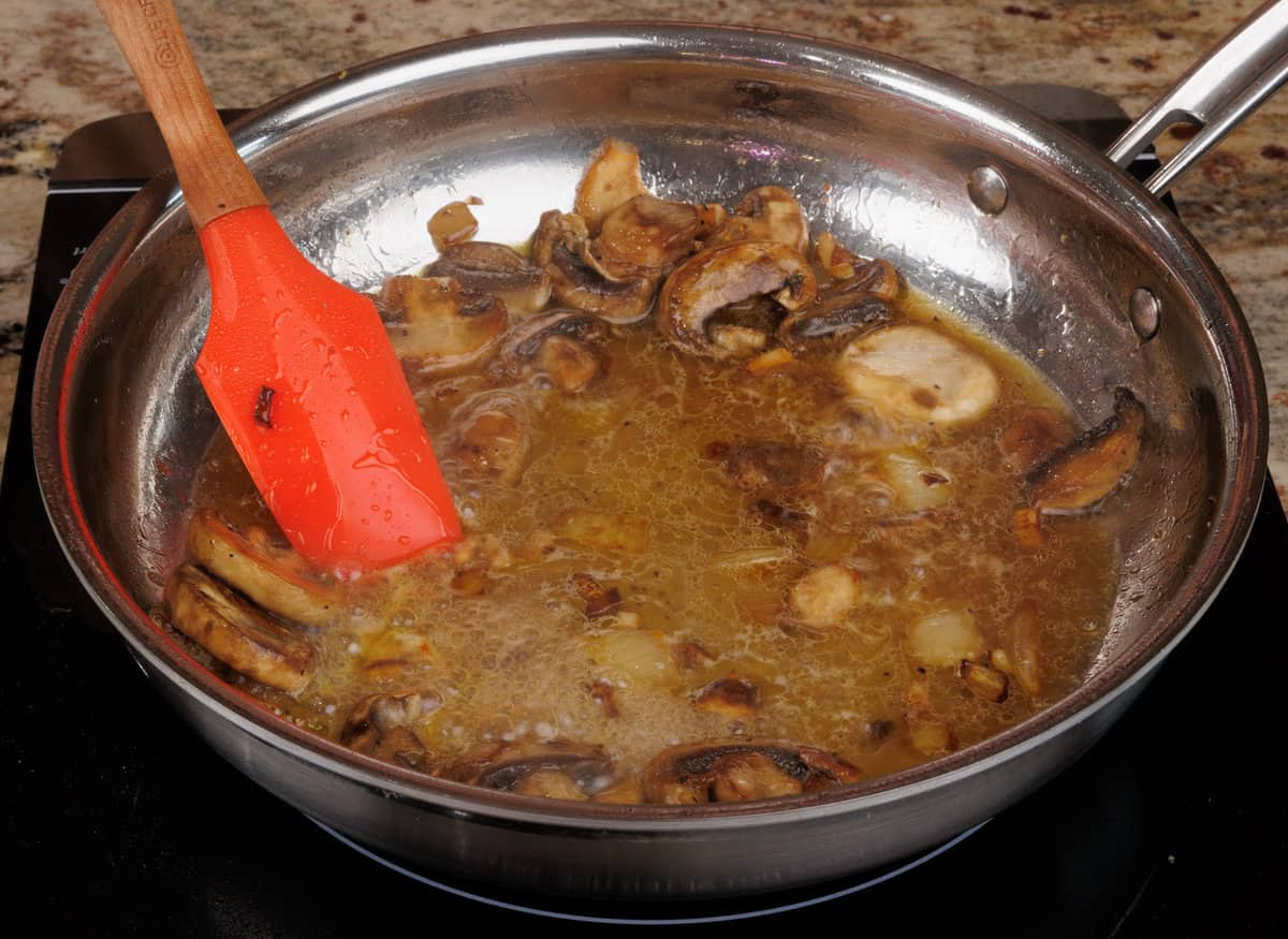 mushrooms simmering in chicken broth in a pan on the stove