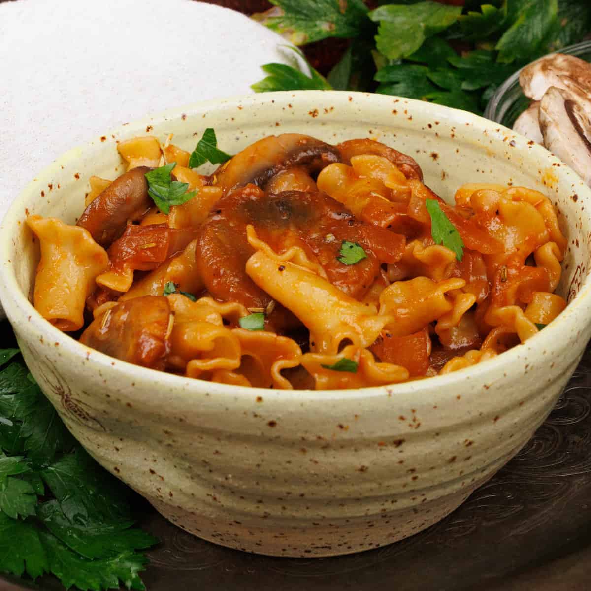 a bowl of creamy mushroom pasta next to a bowl of fresh mushrooms and fresh parsley