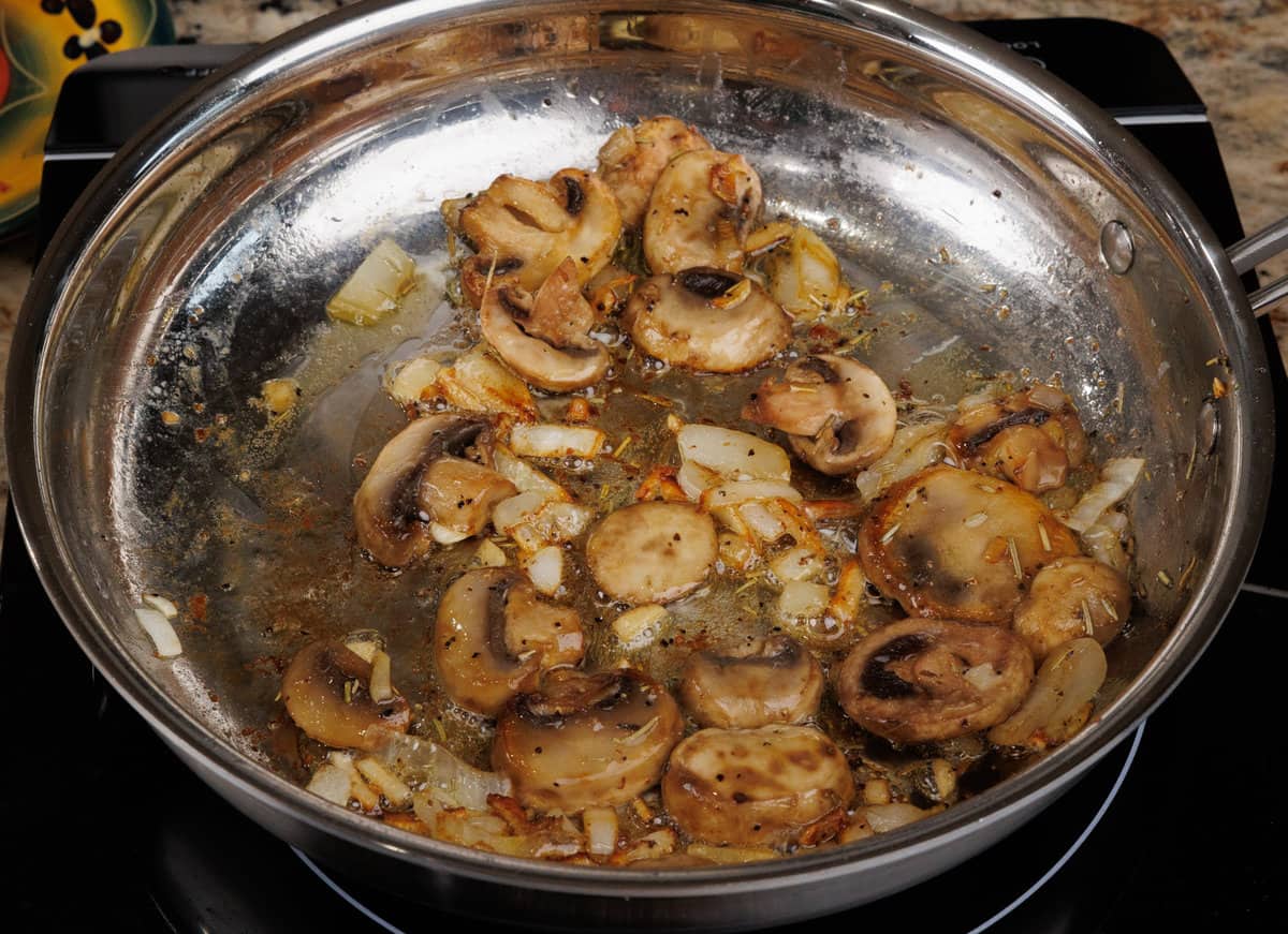 sliced mushrooms cooking in a pan with olive oil, garlic, and onions