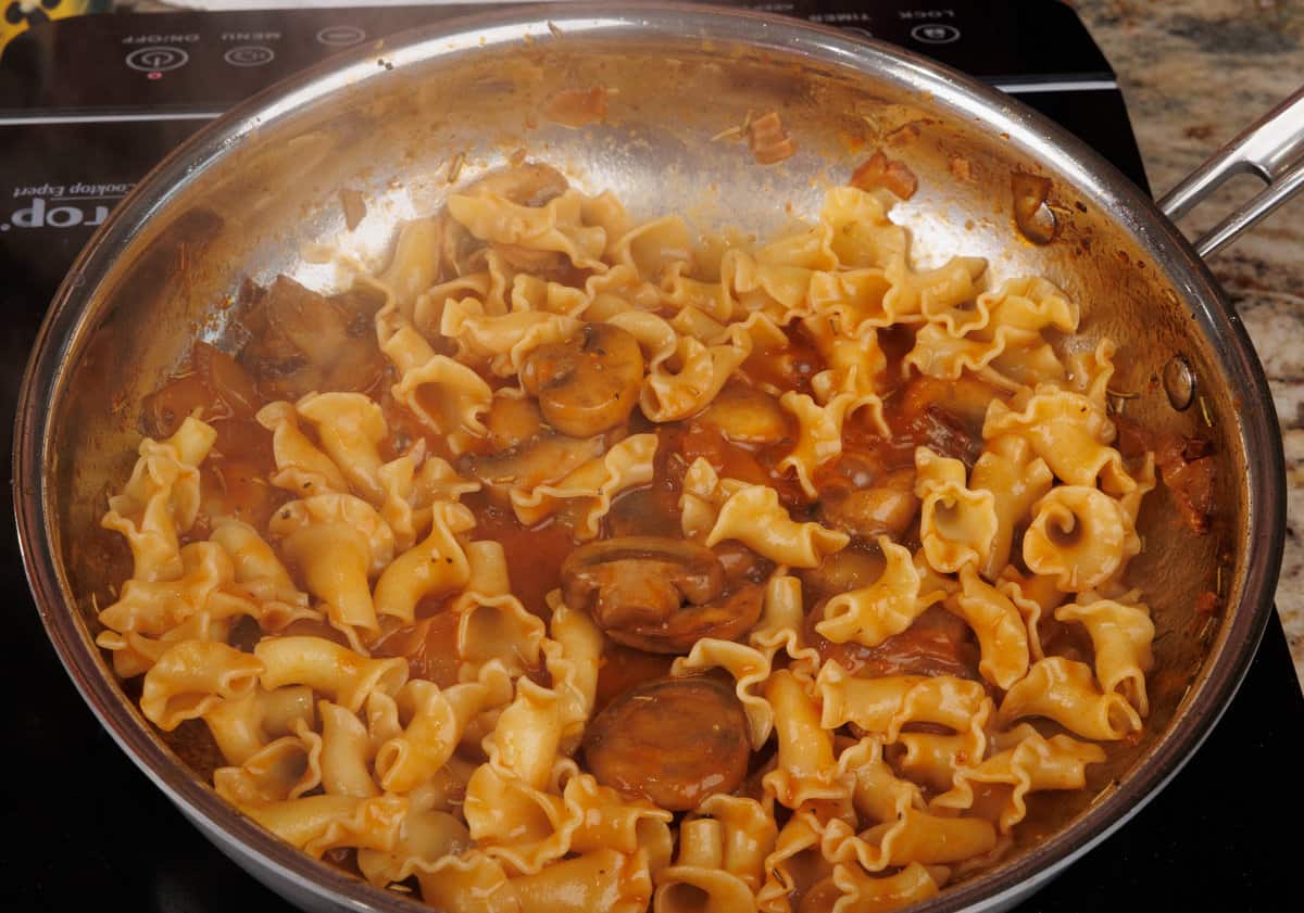 pasta cooking in mushroom sauce in a small skillet