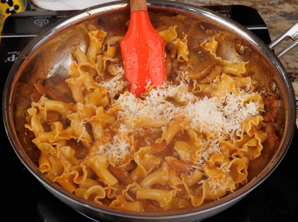 parmesan cheese stirred into pasta with mushroom sauce in a skillet