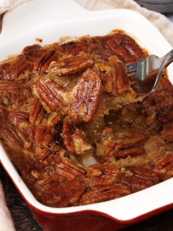 an individual pecan pie with maple syrup in a dish with a fork on the side.