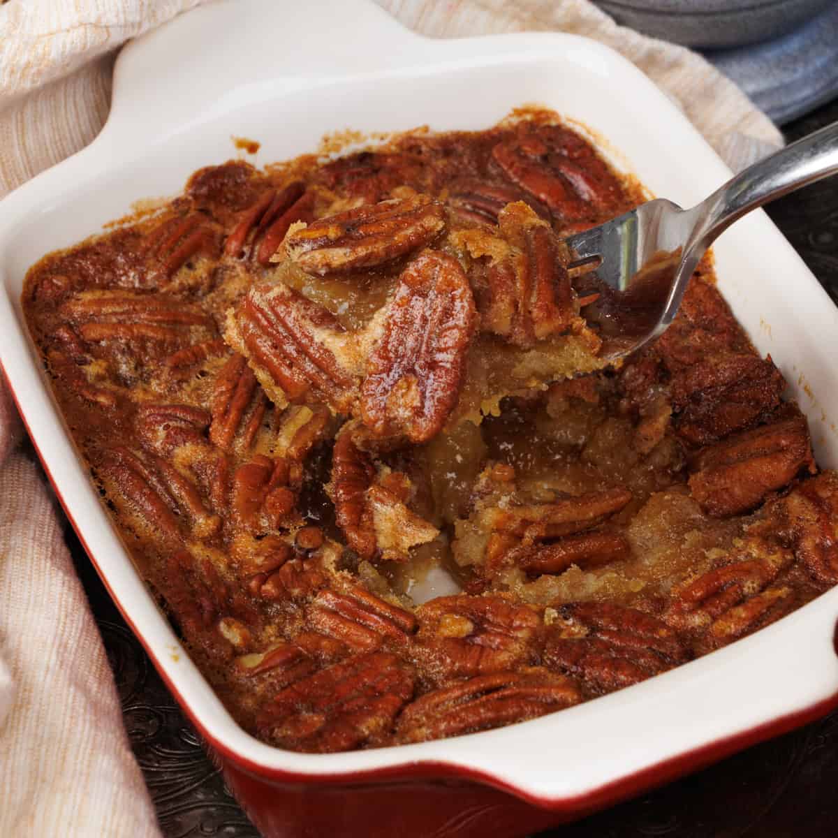 an individual pecan pie with maple syrup in a dish with a fork on the side.
