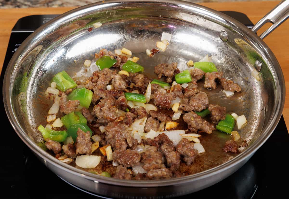 italian sausage, onions, garlic, and green bell peppers cooking in a skillet