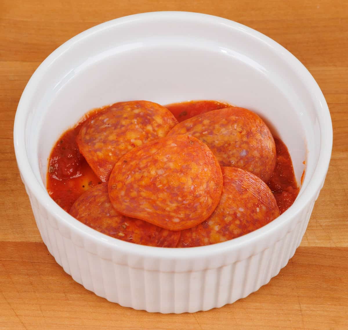 5 slices of pepperoni on the bottom of a small white dish