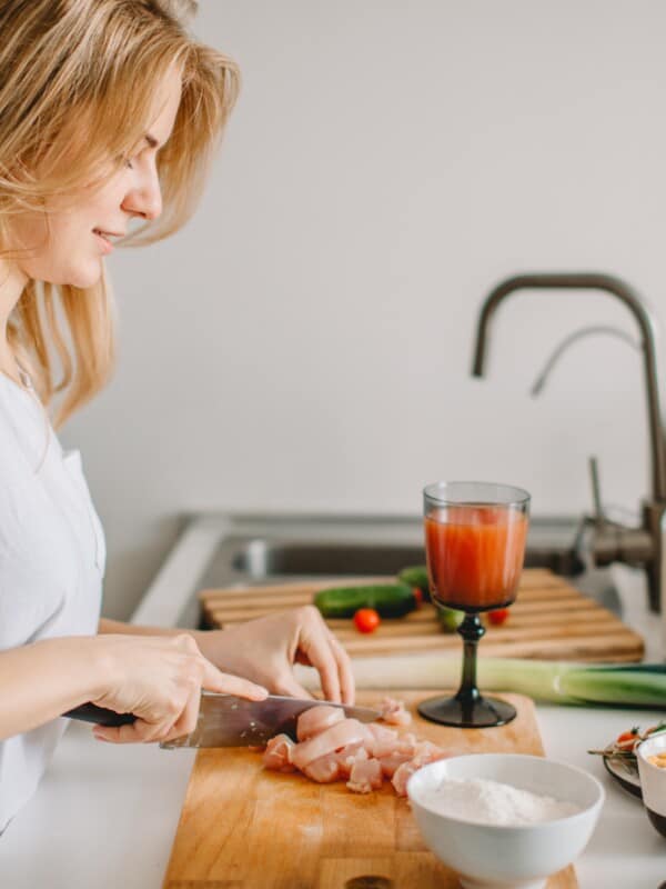 a blonde woman in a kitchen chopping vegetables to prepare a meal