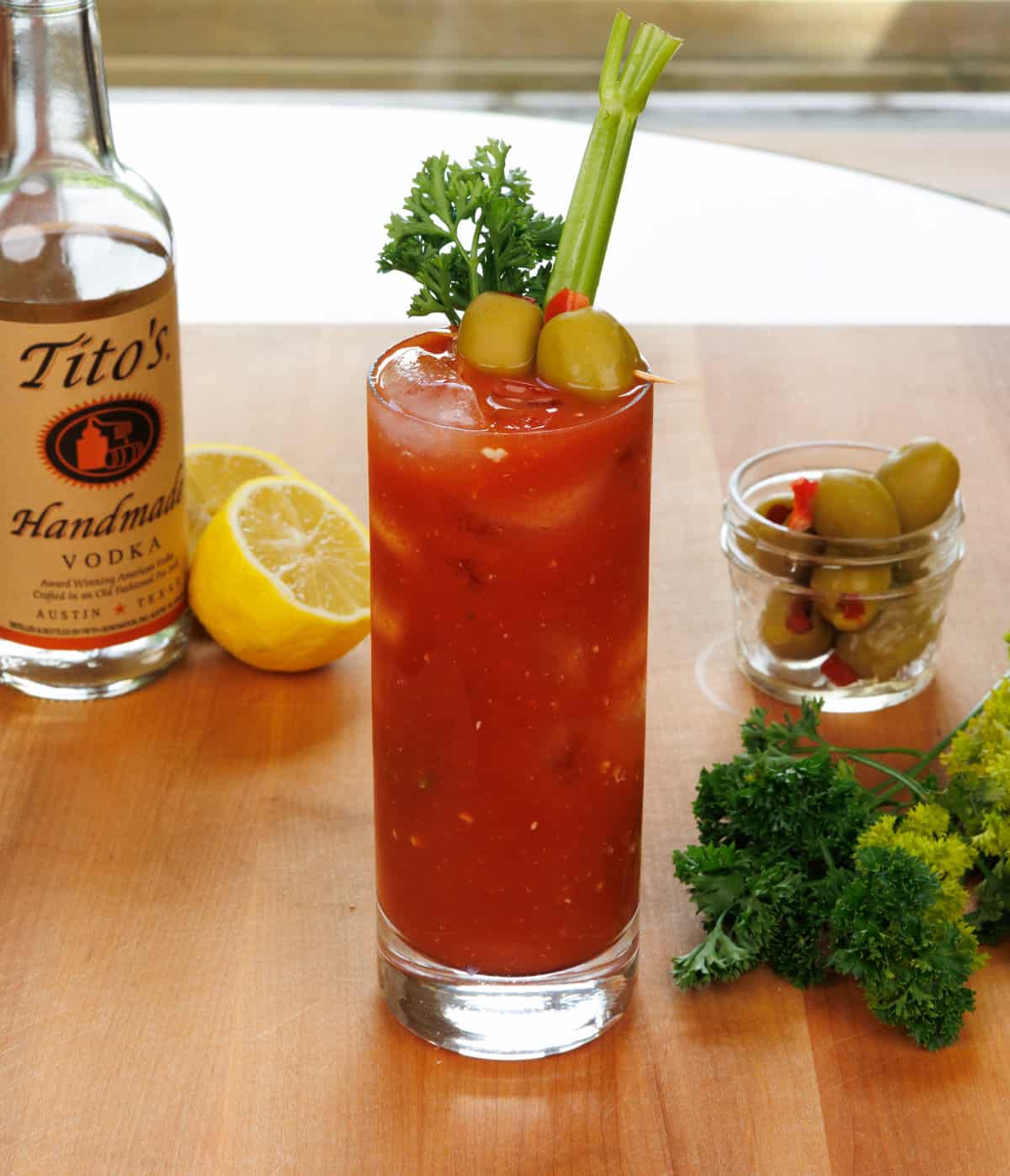 a bloody mary on a table next to a bottle of vodka and parsley