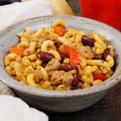 a bowl of chili mac next to a white napkin.