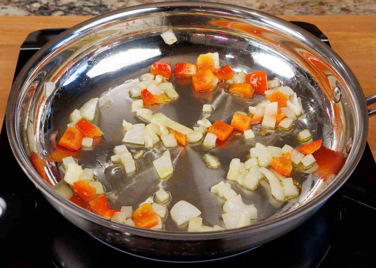 chopped onions and red bell peppers in a skillet.