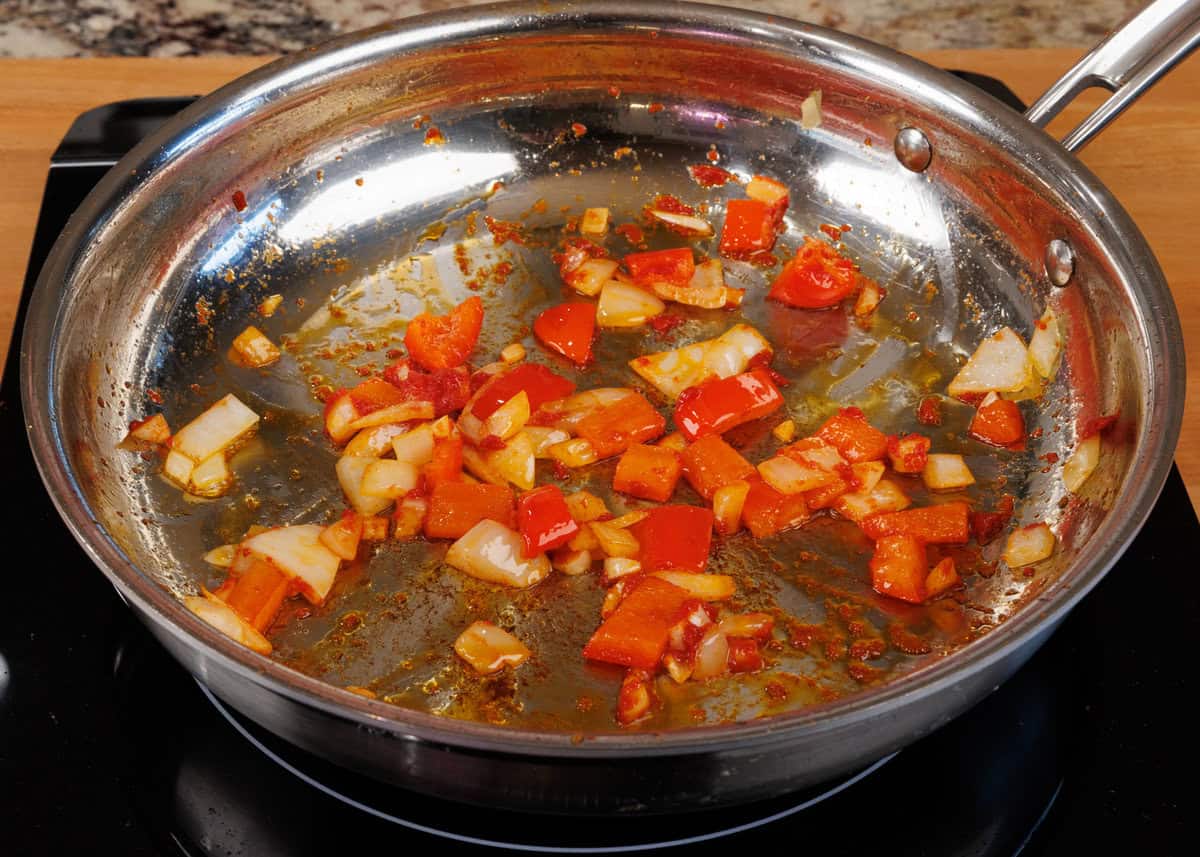 onions, garlic, bell peppers, and tomato pasta cooking in a skillet on the stove.