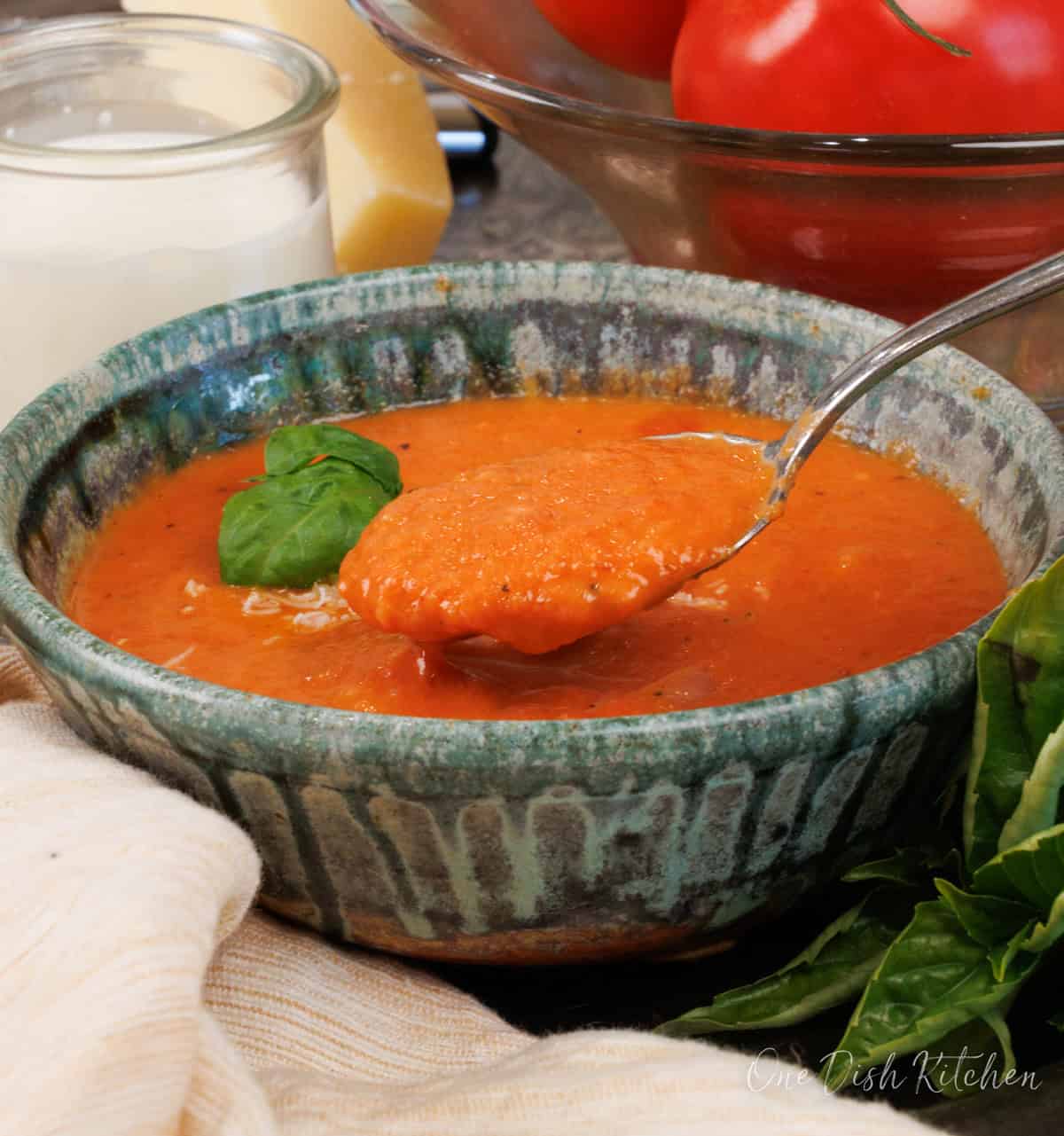 a single serving of creamy tomato soup in a bowl with a spoon on the side.