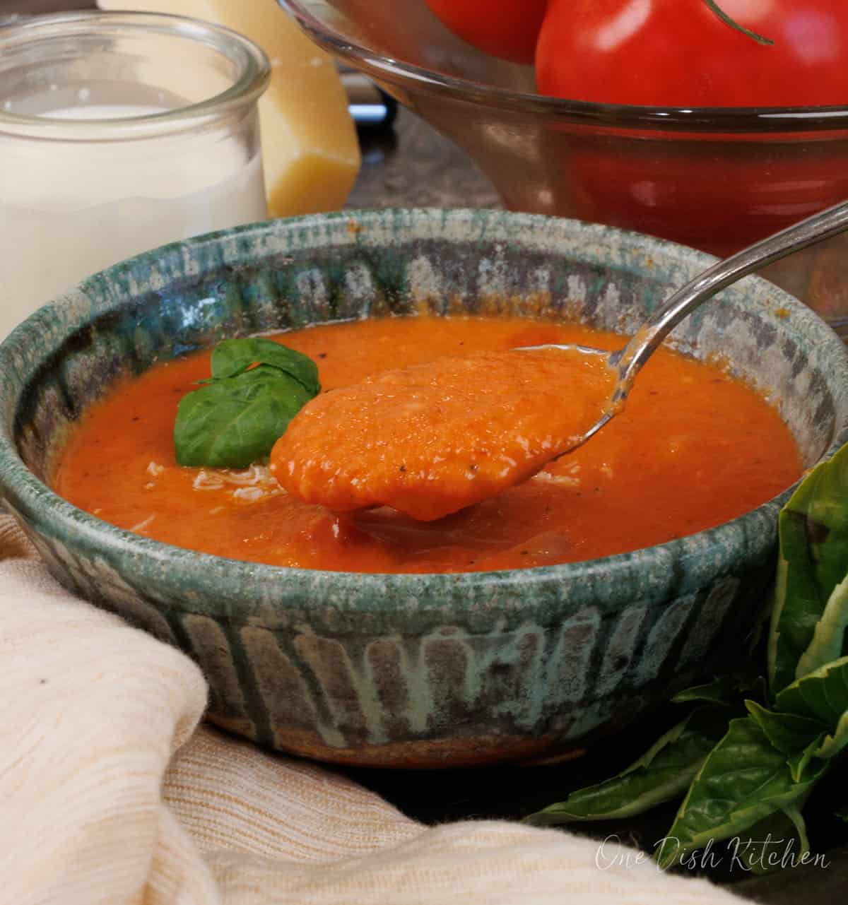 creamy tomato soup topped with grated parmesan cheese with a spoon scooping some soup.
