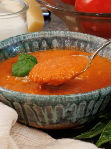 a bowl of creamy tomato soup topped with fresh basil and a spoon of the soup above the bowl