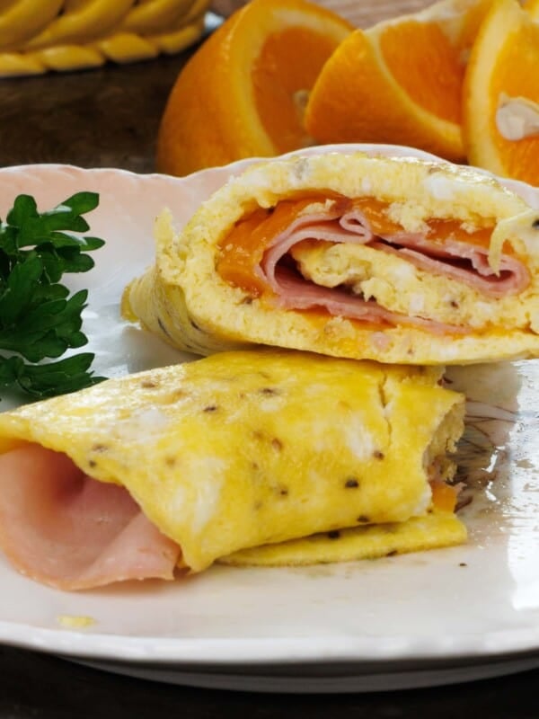 an egg wrap filled with ham and cheddar cheese on a white plate next to a plate of sliced oranges