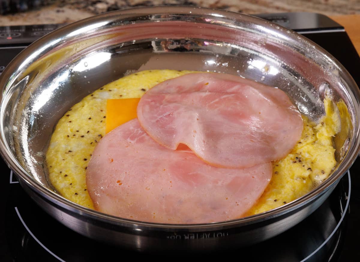 ham and cheese on top of eggs cooking in a skillet