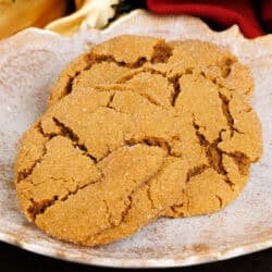 three molasses cookies on a white plate next to Christmas greenery and a red napkin on a silver tray.