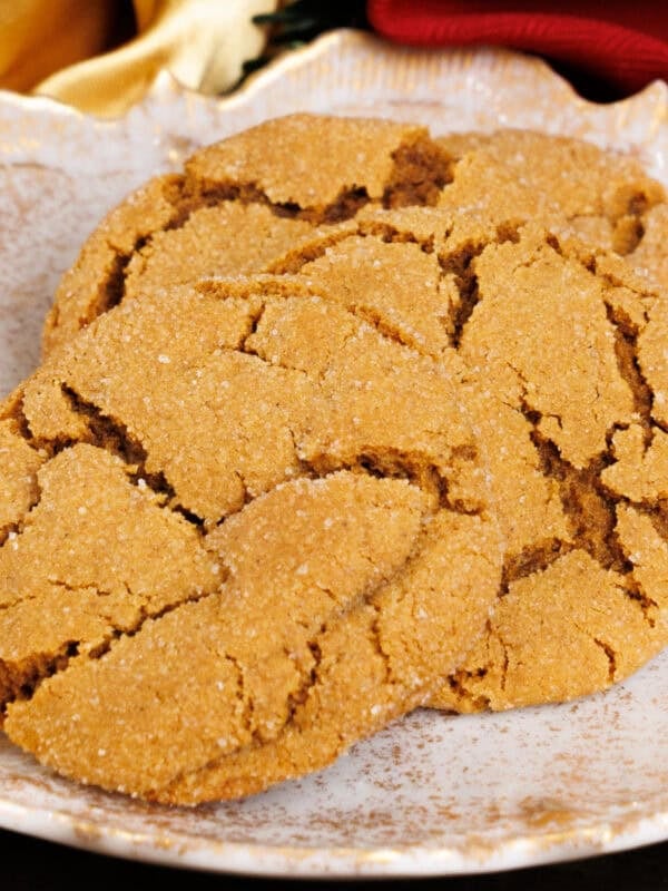 three molasses cookies on a white plate next to Christmas greenery and a red napkin on a silver tray.