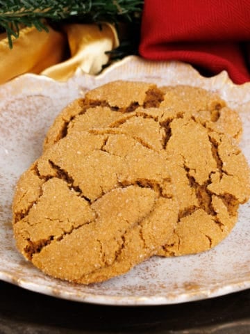three molasses cookies on a white plate next to Christmas greenery and a red napkin on a silver tray