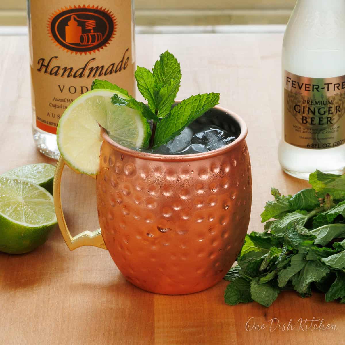 a moscow mule in a copper mug with the ingredients needed on a wooden table