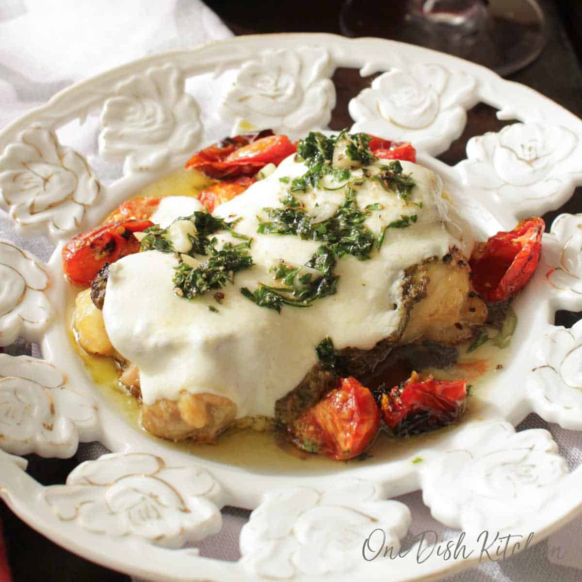 chicken topped with tomatoes and mozzarella cheese on a white plate.