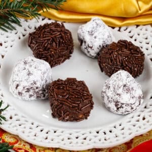 a small batch of rum balls rolled in powdered sugar and sprinkles on a white plate.
