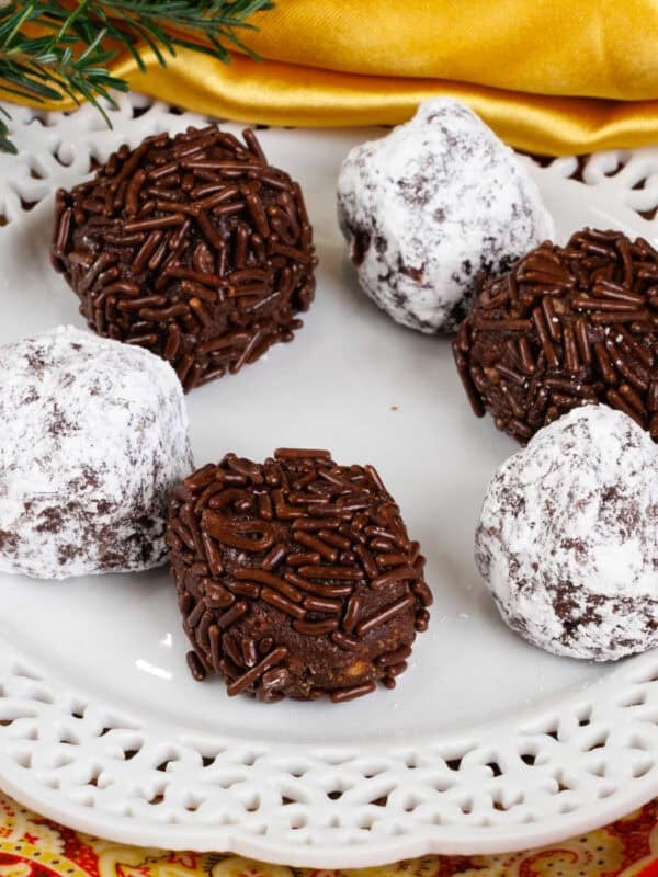 a small batch of rum balls rolled in powdered sugar and sprinkles on a white plate.