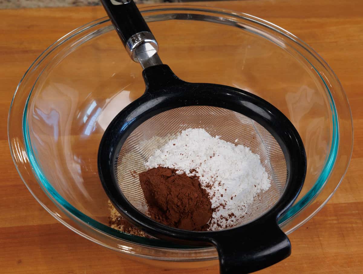 sifting powdered sugar and cocoa powder in a fine mesh strainer over a bowl