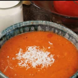 a green bowl filled with creamy tomato soup topped with grated parmesan cheese next to a bowl of fresh tomatoes