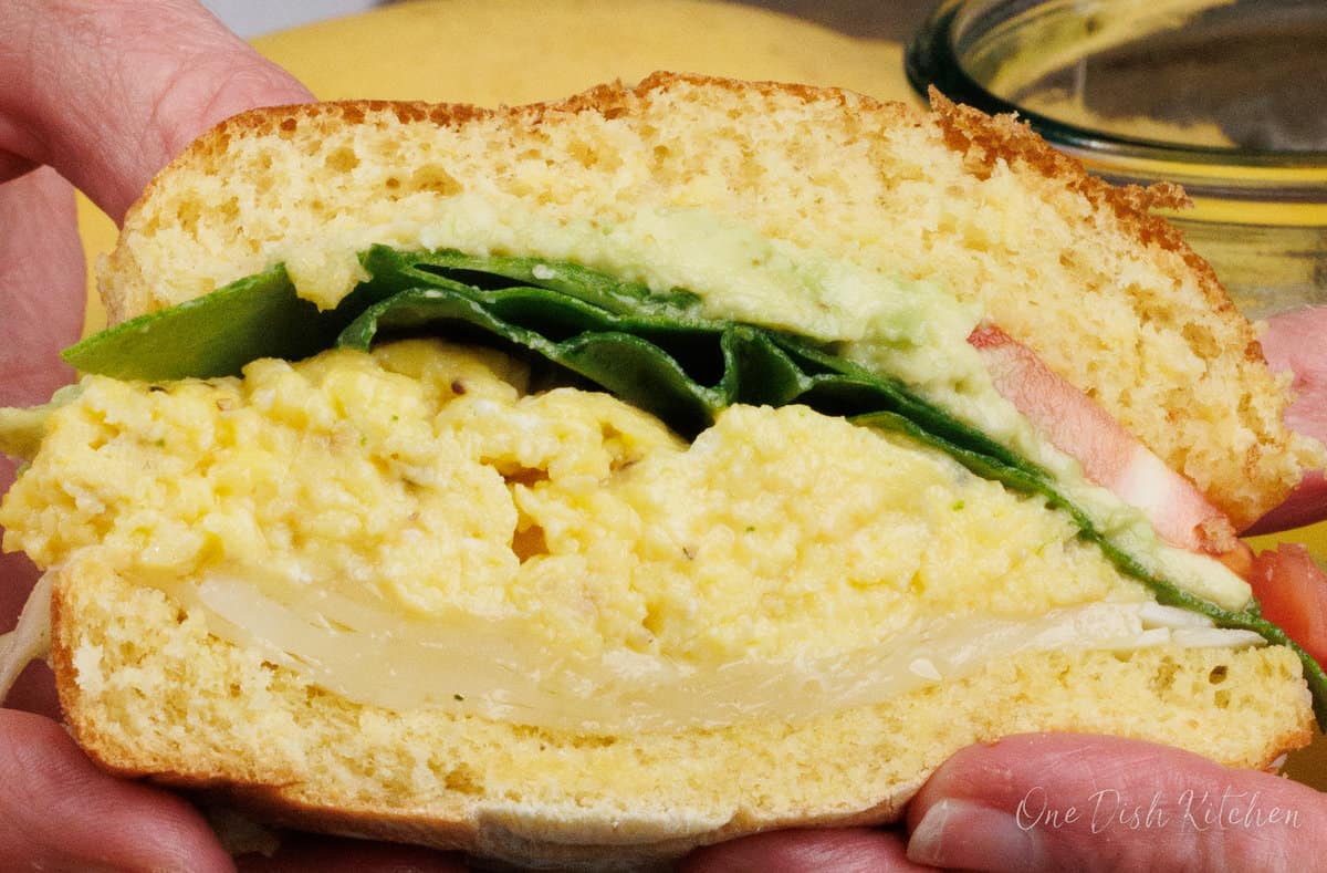 half of an egg and avocado breakfast sandwich held by two hands