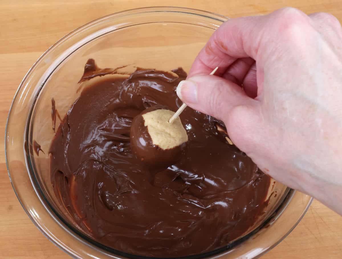 dipping a peanut butter ball into a bowl of melted chocolate