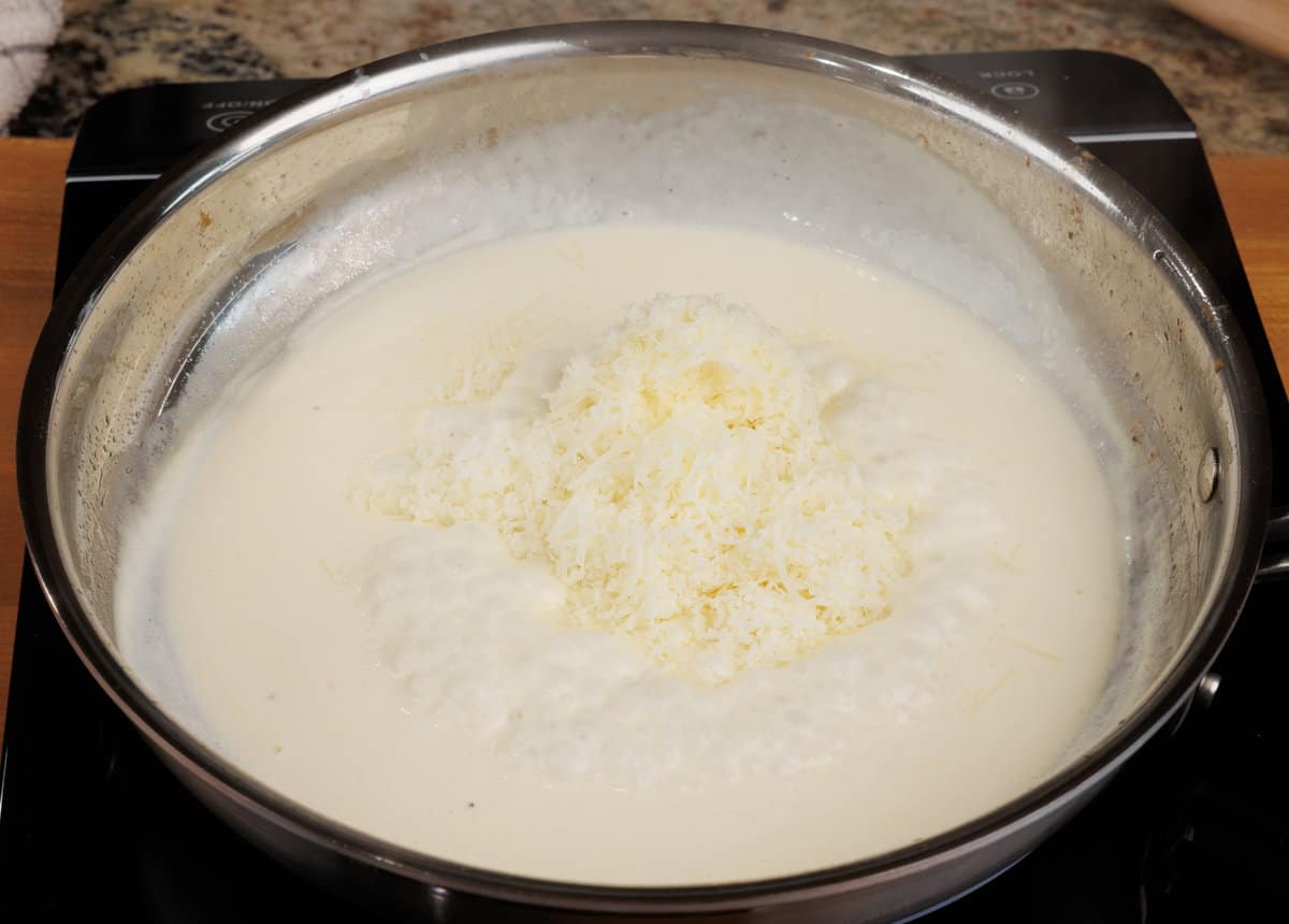 fresh parmesan cheese added to a cream sauce in a skillet
