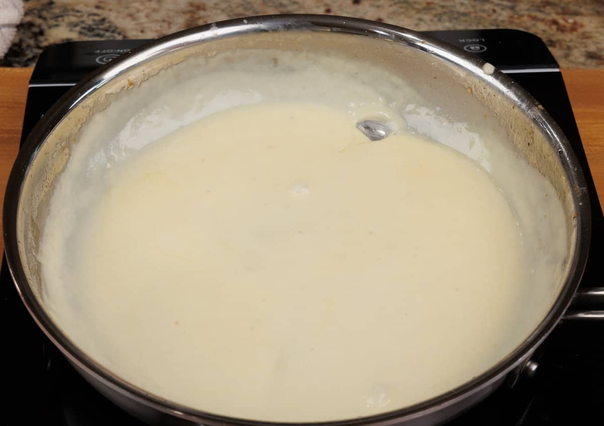 homemade alfredo sauce simmering in a small skillet on the stove